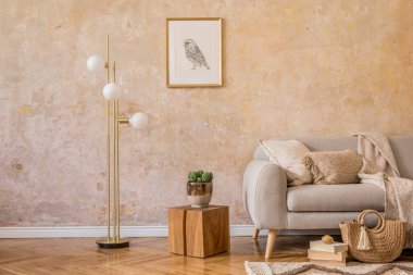 Tasarım gri kanepe, ahşap sehpa, raf, küp, halı, rattan kesesi, bitkiler, resim çerçevesi, masa lambası ve ev dekorunda zarif aksesuarlar ile oturma odasının iç kısımlarında şık bir skandi kompozisyonu..