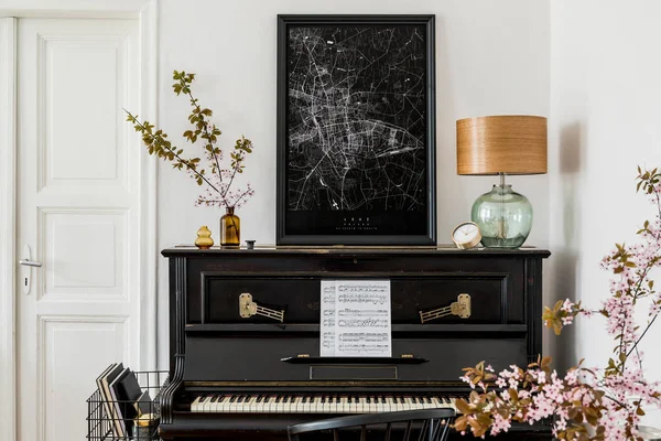 Stylish composition at living room interior with black piano, mock up poster map, dried flowers, gold clock, design lamp and elegant presonal accessories in modern home decor.