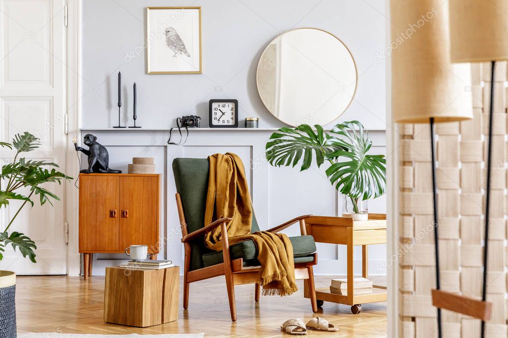 Stylish interior of living room with design armchair, wooden vintage commode, round mirror, shelf, tropical leaves, coffee table, decoration, carpet and persnoal accessories in home decor.
