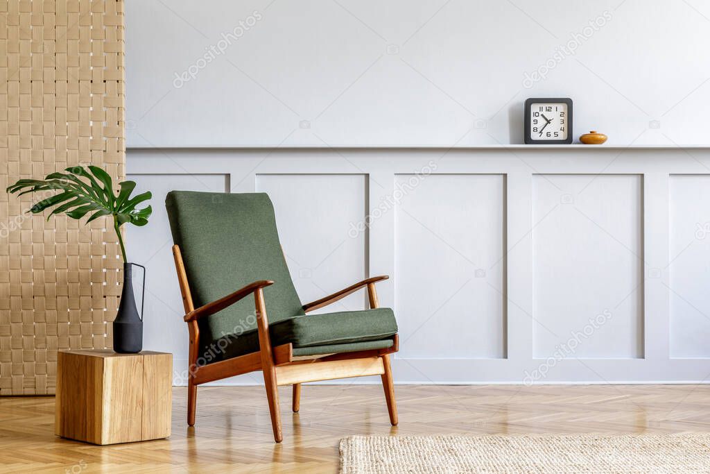 Minimalistic composition at living room interior with design green armchair, beige panel, plants, cube, shelf, copy space, decoration and elegant personal accessories in stylish home decor.