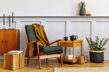 Kaliteli yeşil koltuk, ahşap sehpa, mobilya, gri duvar, raf, halı, bitki, dekor, kitap, kopyalama alanı ve zarif kişisel aksesuarları olan iç tasarım oturma odası..