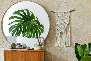 Modern retro iç mekan tasarım klozeti, vazoda tropikal yaprak, yuvarlak ayna, beyaz makrome, kitap, grunge duvar ve şık ev dekorunda zarif aksesuarlar.