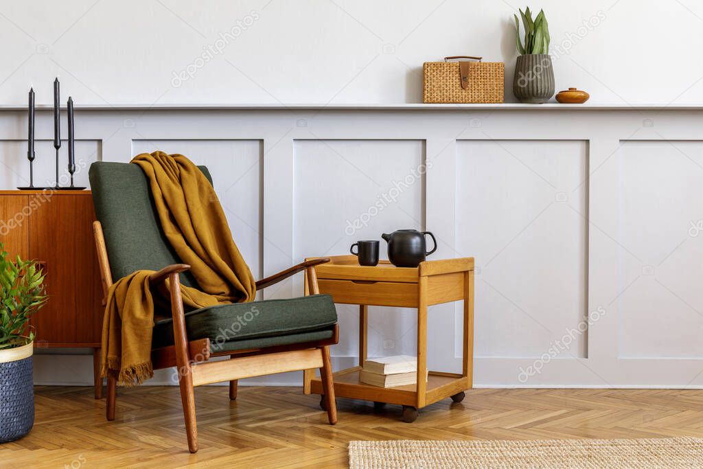 Interior design of stylish living room with vintage green armchair, wooden coffee table, teapot, furniture, grey wall, shelf, carpet, plant, book, copy space and elegant personal accessories.