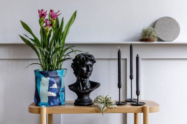Minimalist oturma odası içinde ahşap konsol, hippi tenceresinde güzel bitkiler, yaprak, kitap, saat, raf, dekorasyon, gri duvar ve şık ev dekorasyonu kişisel aksesuarlar.