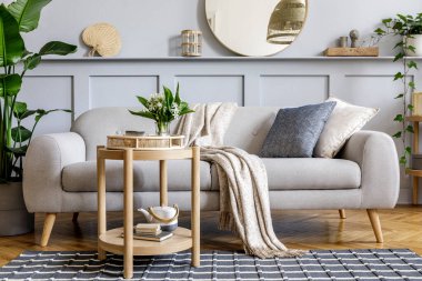 Tasarım gri kanepe, ahşap sehpa, tropikal bitkiler, raf, ayna, mobilya, ekose yastık, çaydanlık, kitap ve ev dekorunda zarif kişisel aksesuarlar ile İskandinav oturma odası.