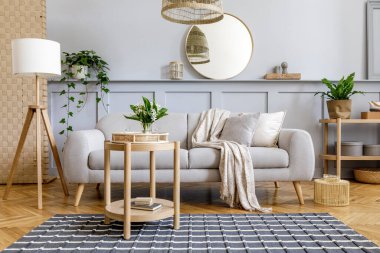 Tasarım gri kanepe, ahşap sehpa, tropikal bitkiler, raf, ayna, mobilya, ekose yastık, çaydanlık, kitap ve ev dekorunda zarif kişisel aksesuarlar ile İskandinav oturma odası.