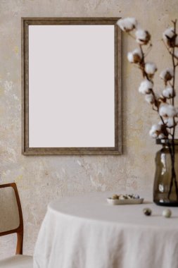 Şık ve zarif bir yemek odası. Lokanta masası, tasarım koltuğu vazoda çiçekler ve zarif bir rattan süslemesi. Poster çerçevesini düzenle. Şablon.