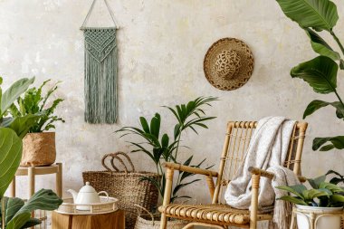 Oturma odasının iç kısmının şık ve çiçekli kompozisyonu içinde rattan koltuklar, tasarım kapları, dekorasyon, makrome ve şık ev dekorasyonu gibi pek çok tropikal bitki var..