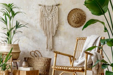 Oturma odasının iç kısmının şık ve çiçekli kompozisyonu içinde rattan koltuklar, tasarım kapları, dekorasyon, makrome ve şık ev dekorasyonu gibi pek çok tropikal bitki var..