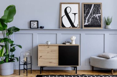 Oturma odasının içinde iki tane poster çerçevesi, ahşap tuvalet, tasarım siyah lamba, bitkiler, dekorasyon, halı ve şık ev dekorasyonuyla şık aksesuarlar var.. 
