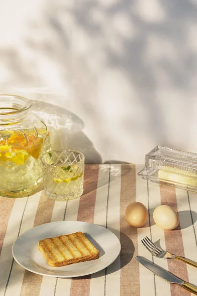 Stylish composition of outdoor kitchen space with wooden table, food, drinks, kitchen accessories, beige tablecloth and summer shadows. Country side mood. Template.