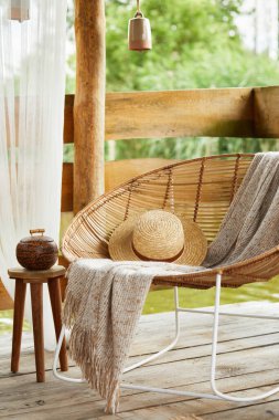 Göl kenarındaki yazlık çardağın iç tasarımı, modern dekorasyonda şık rattan koltuklar, sehpa, kanepe, yastıklar, ekose ve zarif aksesuarlar. Yaz titreşimleri. Sakinleş. Şablon.