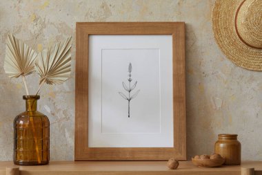 Oturma odasının içi. Poster çerçevesi, zarif aksesuarlar, vazoda kurumuş çiçekler, ahşap konsol ve şık ev dekorunda asılı bir şapka..