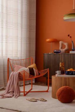 Turuncu kablo koltuk, rahat tekstil ve heykel aksanlı modern köşe. Doğal ışık ve koyu renk kontrastı dengeli ve davetkar bir görünüm yaratır.