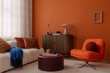 Beyaz kanepeli şık bir oturma odası, turuncu aksanlı sandalye, ve katmanlı yastıklar ve zengin dokular. Canlı turuncu bir duvar, cesur ve sıcak bir zemin görevi görür..