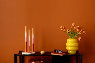 Renkli raf şekillendirmesi, ombr mumları, parlak sarı vazolar, laleler ve turuncu bir duvara karşı minimalist aksesuarlar. Boşluğu kopyala.