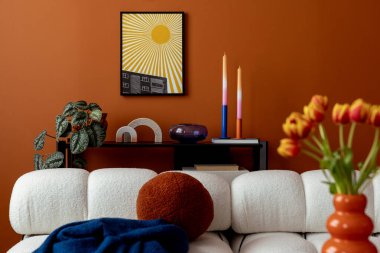 Turuncu duvarlı modern oturma odası, poster resimleri, beyaz kanepe, renkli mumlar ve dekoratif nesneler..