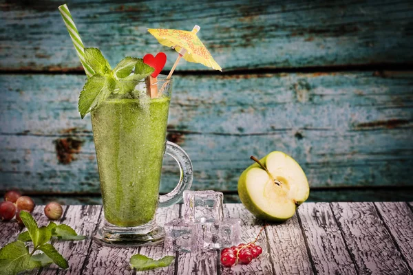 green smoothie in a glass tumbler on a table with green apple and berries