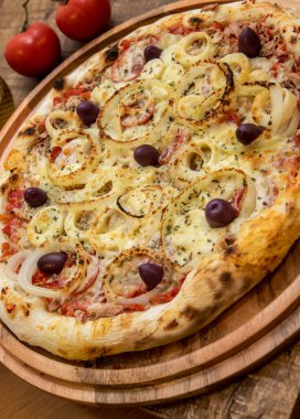 Ton balıklı İtalyan pizzası mutfakta ya da pizzacıda dilimlenmemiş bir tahta üzerinde servis edilir.