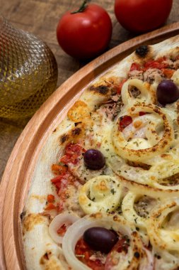 Ton balıklı İtalyan pizzası mutfakta ya da pizzacıda dilimlenmemiş bir tahta üzerinde servis edilir.