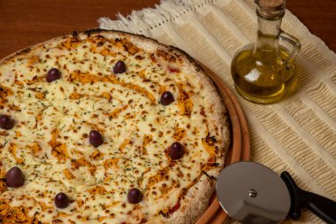 Tahta bir tahtanın üzerinde servis edilen Pizza Tavuk Katupiry aroması. Mozzarella, tavuk, krem peynirli, zeytinli ve kırmızı domates soslu. Bir bardak zeytinyağı. Geleneksel Brezilya pizzası.