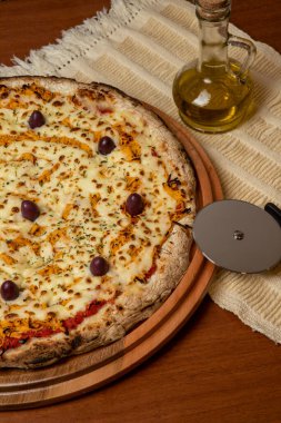 Tahta bir tahtanın üzerinde servis edilen Pizza Tavuk Katupiry aroması. Mozzarella, tavuk, krem peynirli, zeytinli ve kırmızı domates soslu. Bir bardak zeytinyağı. Geleneksel Brezilya pizzası.