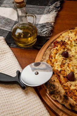 Tahta bir tahtanın üzerinde servis edilen Pizza Tavuk Katupiry aroması. Mozzarella, tavuk, krem peynirli, zeytinli ve kırmızı domates soslu. Bir bardak zeytinyağı. Geleneksel Brezilya pizzası.
