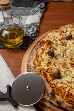 Tahta bir tahtanın üzerinde servis edilen Pizza Tavuk Katupiry aroması. Mozzarella, tavuk, krem peynirli, zeytinli ve kırmızı domates soslu. Bir bardak zeytinyağı. Geleneksel Brezilya pizzası.