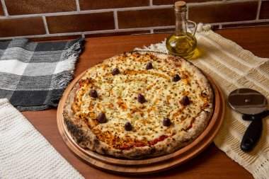 Tahta bir tahtanın üzerinde servis edilen Pizza Tavuk Katupiry aroması. Mozzarella, tavuk, krem peynirli, zeytinli ve kırmızı domates soslu. Bir bardak zeytinyağı. Geleneksel Brezilya pizzası.