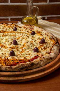 Tahta bir tahtanın üzerinde servis edilen Pizza Tavuk Katupiry aroması. Mozzarella, tavuk, krem peynirli, zeytinli ve kırmızı domates soslu. Bir bardak zeytinyağı. Geleneksel Brezilya pizzası.