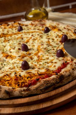 Tahta bir tahtanın üzerinde servis edilen Pizza Tavuk Katupiry aroması. Mozzarella, tavuk, krem peynirli, zeytinli ve kırmızı domates soslu. Bir bardak zeytinyağı. Geleneksel Brezilya pizzası.