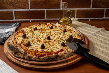 Tahta bir tahtanın üzerinde servis edilen Pizza Tavuk Katupiry aroması. Mozzarella, tavuk, krem peynirli, zeytinli ve kırmızı domates soslu. Bir bardak zeytinyağı. Geleneksel Brezilya pizzası.