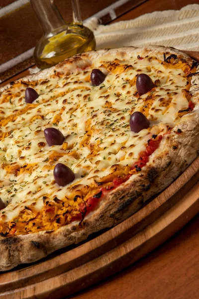 Tahta bir tahtanın üzerinde servis edilen Pizza Tavuk Katupiry aroması. Mozzarella, tavuk, krem peynirli, zeytinli ve kırmızı domates soslu. Bir bardak zeytinyağı. Geleneksel Brezilya pizzası.