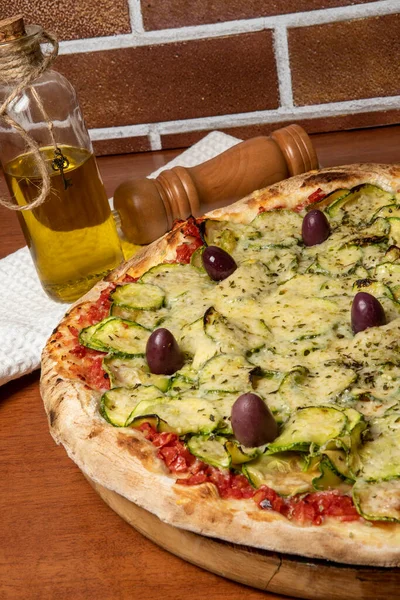 Lezzetli İtalyan vejetaryen pizzası, domates sosu, biber, zeytin ve ahşap masa arkasında kabak. Portekizce metin: dinginlik