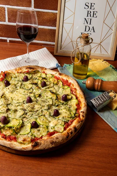 Lezzetli İtalyan vejetaryen pizzası, domates sosu, biber, zeytin ve ahşap masa arkasında kabak. Portekizce metin: dinginlik