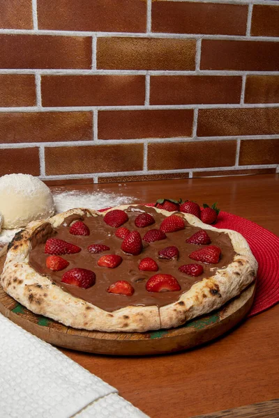 Chocolate pizza and strawberries on wooden table