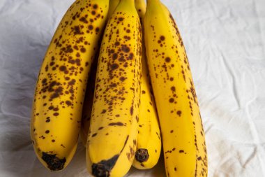 Beyaz kırışık masa örtüsü üzerinde koyu benekli olgun bir muz.