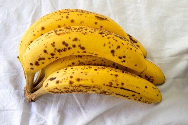 Beyaz kırışık masa örtüsü üzerinde koyu benekli olgun bir muz.