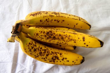 Beyaz kırışık masa örtüsü üzerinde koyu benekli olgun bir muz.