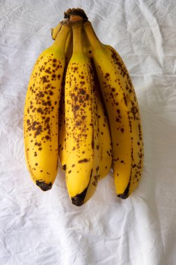 Beyaz kırışık masa örtüsü üzerinde koyu benekli olgun bir muz.