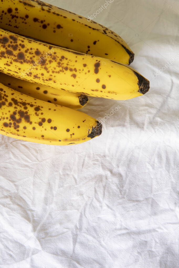 Ripe banana with dark spots on white wrinkled tablecloth