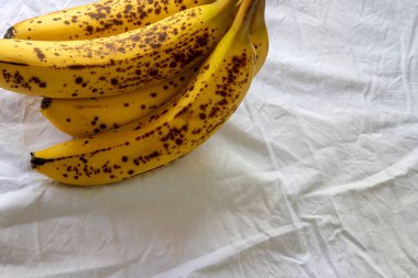 Beyaz kırışık masa örtüsü üzerinde koyu benekli olgun bir muz.