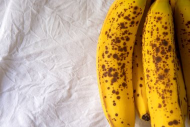 Beyaz kırışık masa örtüsü üzerinde koyu benekli olgun bir muz.