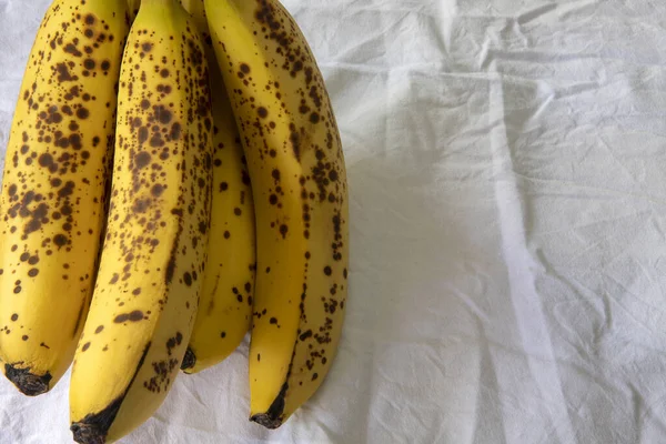 Beyaz kırışık masa örtüsü üzerinde koyu benekli olgun bir muz.