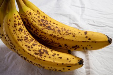 Beyaz kırışık masa örtüsü üzerinde koyu benekli olgun bir muz.