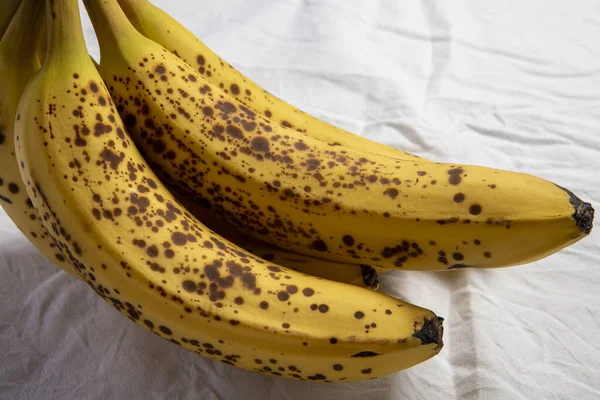 Beyaz kırışık masa örtüsü üzerinde koyu benekli olgun bir muz.