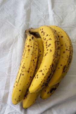 Beyaz kırışık masa örtüsü üzerinde koyu benekli olgun bir muz.