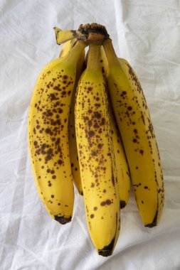 Beyaz kırışık masa örtüsü üzerinde koyu benekli olgun bir muz.