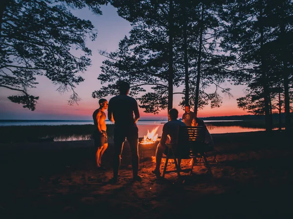 一群年轻快乐的朋友坐在夏日海滩的炉火旁 — 图库照片