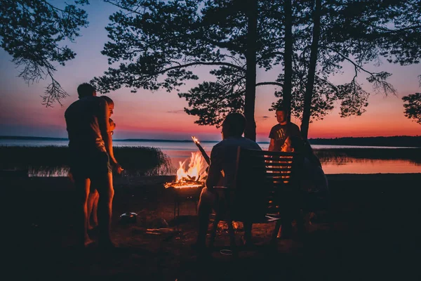 Skupina mladých šťastný přátel sedí u ohně v létě beach — Stock fotografie